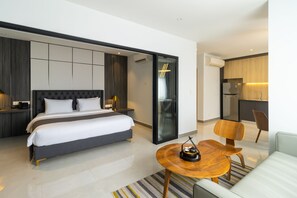 Una habitación de hotel moderna con una cama grande, una pequeña mesa de comedor, un sofá y una zona de cocina.