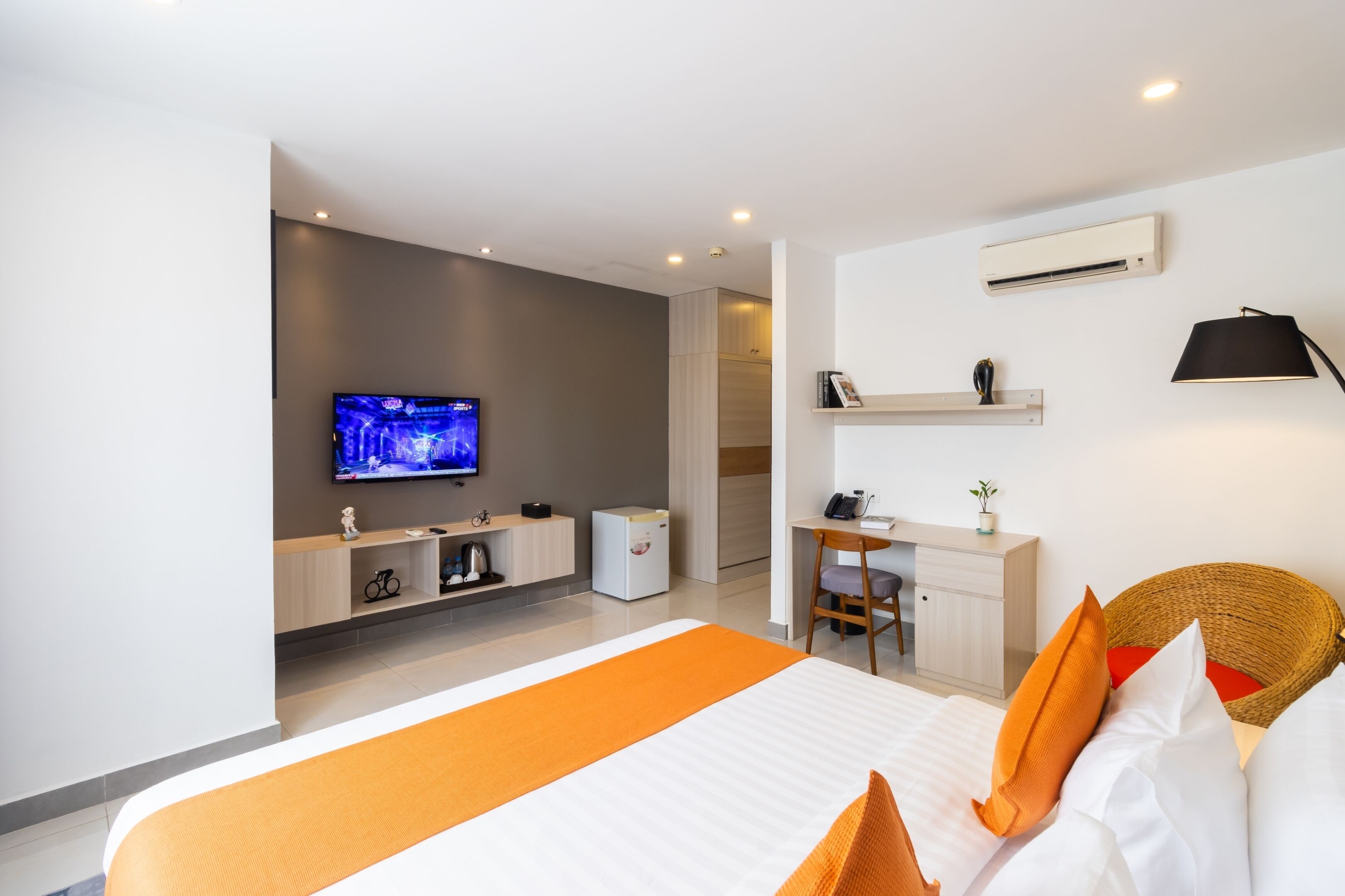 Une chambre d’hôtel moderne équipée d’un grand lit, d’une télévision, d’un bureau et d’un fauteuil en osier.