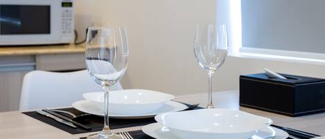 A dining table set with white plates, two wine glasses, and cutlery. A black tissue box is on the table.