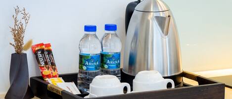 Una bandeja con un paquete de café Nescafé, dos botellas de agua Aruna, una tetera eléctrica plateada y tazas blancas sobre una encimera de cocina.