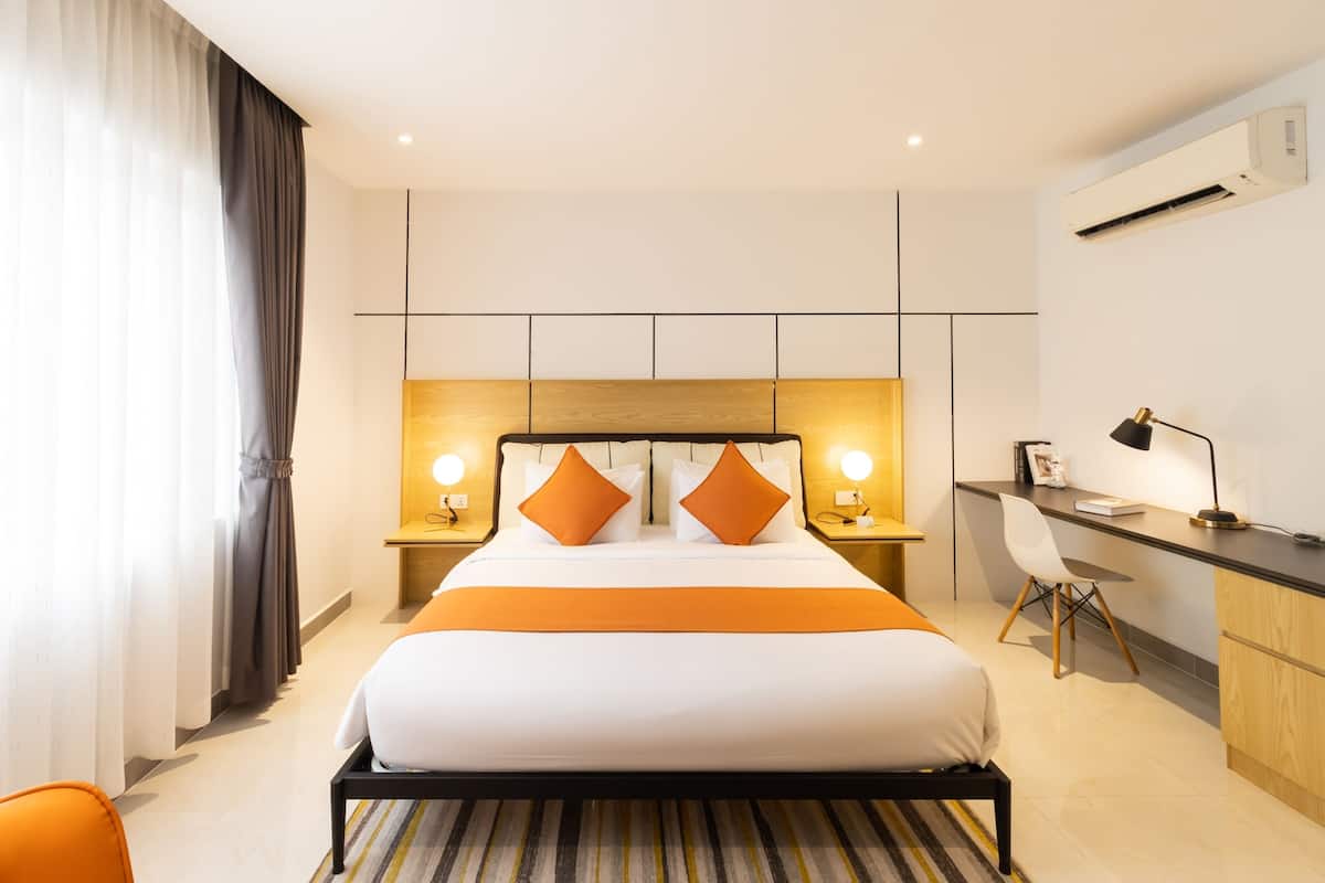 A hotel room with a large bed, a desk, and a chair. There are two bedside tables with lamps.