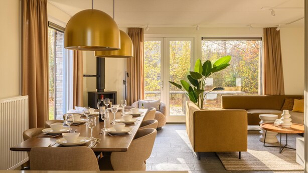 Un comedor con una mesa larga dispuesta para seis comensales, un sofá y una planta grande.