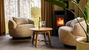 Un rincón acogedor con dos sillones tapizados, una mesita de madera con una botella y copas, y una chimenea.