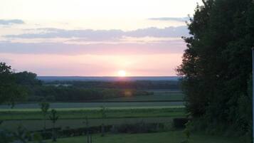 Ein Sonnenuntergang über einer ländlichen Landschaft mit Feldern und Bäumen.