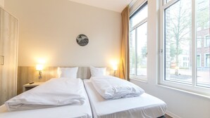 A hotel room with two beds, a nightstand, a wall clock, and a window with curtains. - Modern Retreat in Maastricht (Maastricht)