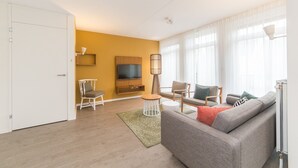 Un salon moderne avec un canapé gris, une table basse en bois et un téléviseur fixé au mur.