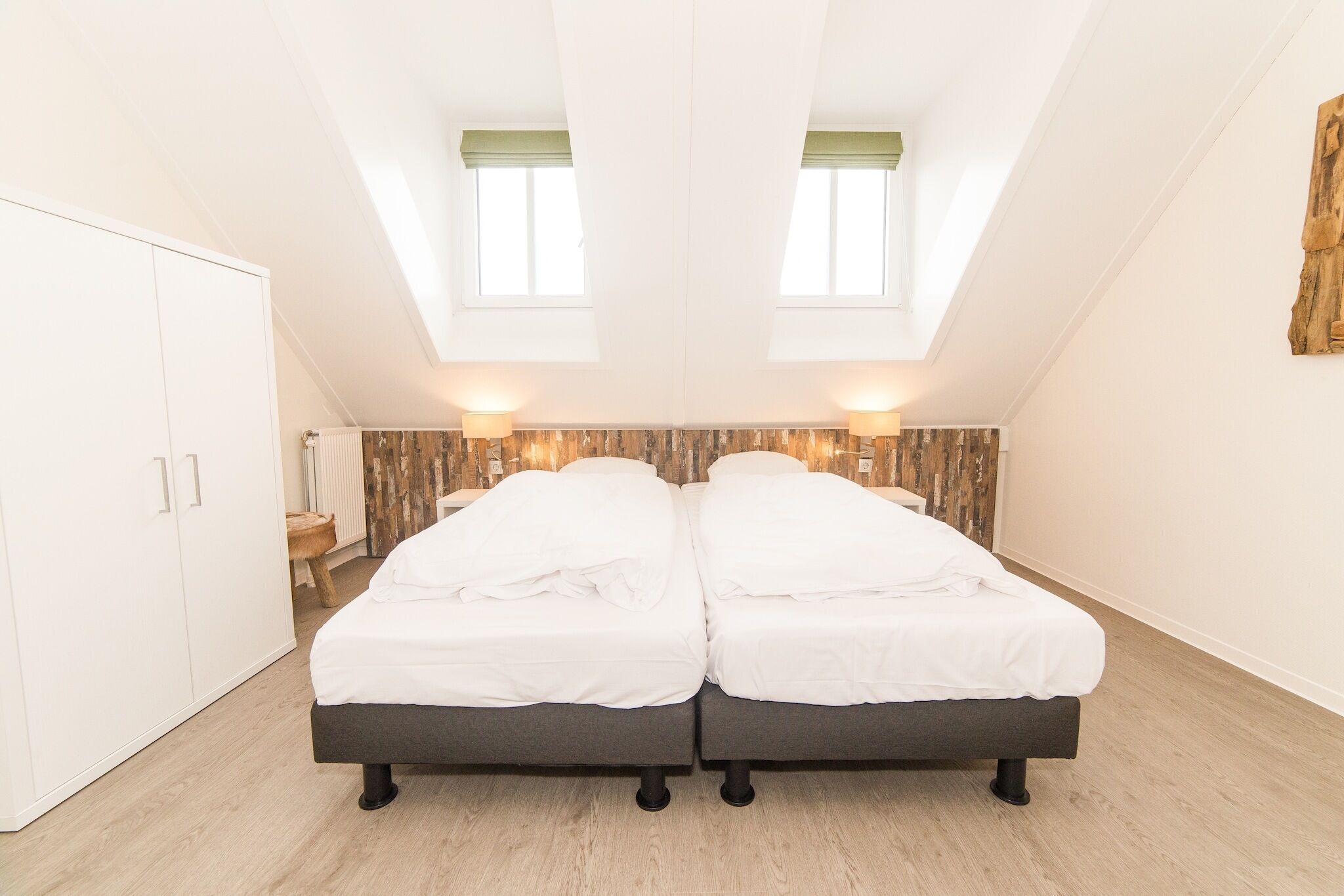 A bedroom with two beds, a wardrobe, a radiator, and a wooden wall panel.