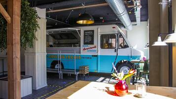 A food truck with a menu board, a wooden table with a vase, and a hanging light fixture.