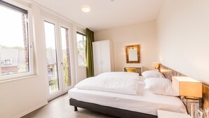 Een slaapkamer met een bed, een kledingkast, een nachtkastje met een lamp en uitzicht door een schuifdeur.
