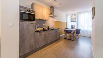 A modern kitchen with a built-in oven, microwave, and stainless steel range hood. There is a dining area with a table and chairs.
