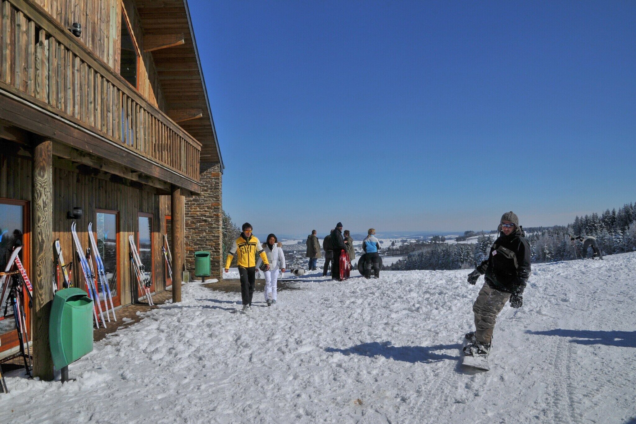 Un bâtiment en bois avec une façade en pierre, une piste de ski et un ciel dégagé.