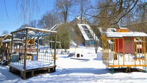 Un parque infantil con juegos cubiertos de nieve y una casa al fondo.