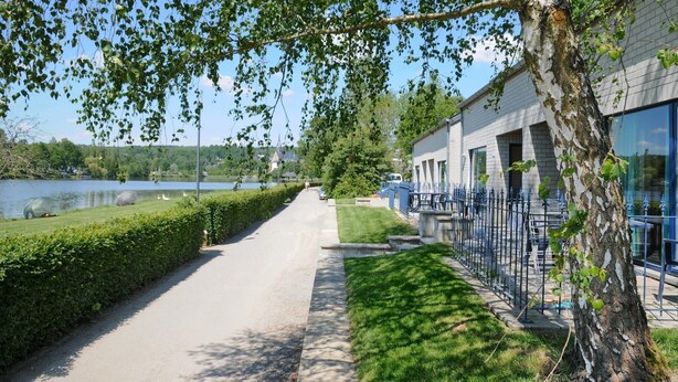 Un camino que lleva a un edificio con vista al lago, un césped cuidado y una valla de metal.