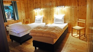 Una habitación tipo cabaña de madera con dos camas, una silla y un ventanal con cortinas.