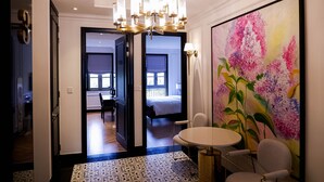A hotel room with a large bed, a dining area with a table and chairs, a chandelier, and a large floral painting on the wall. - Maison d'Rose (Phu Quoc)