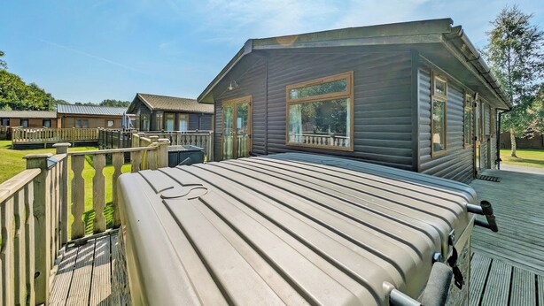 A wooden cabin with a deck, large windows, and a metal roof.