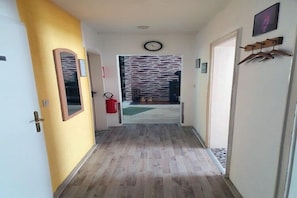 A hallway with a wooden floor, a clock on the wall, and a door on the right.