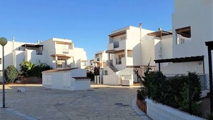 A residential area with modern white buildings, a paved courtyard, and a small white structure. - Duplex in Urb Naturista by the Beach (Vera Playa)