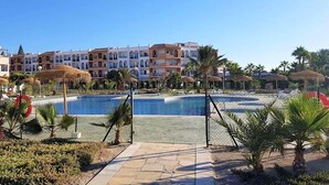 A resort with a swimming pool, palm trees, and a row of multi-story buildings with balconies. - Duplex in Urb Naturista by the Beach (Vera Playa)
