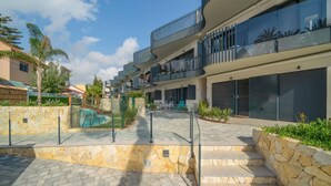A modern multi-story building with balconies, a swimming pool, and stone pathways.