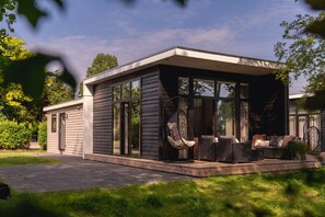 Une maison moderne dotée d’un patio couvert, de grandes fenêtres et de mobilier d’extérieur.