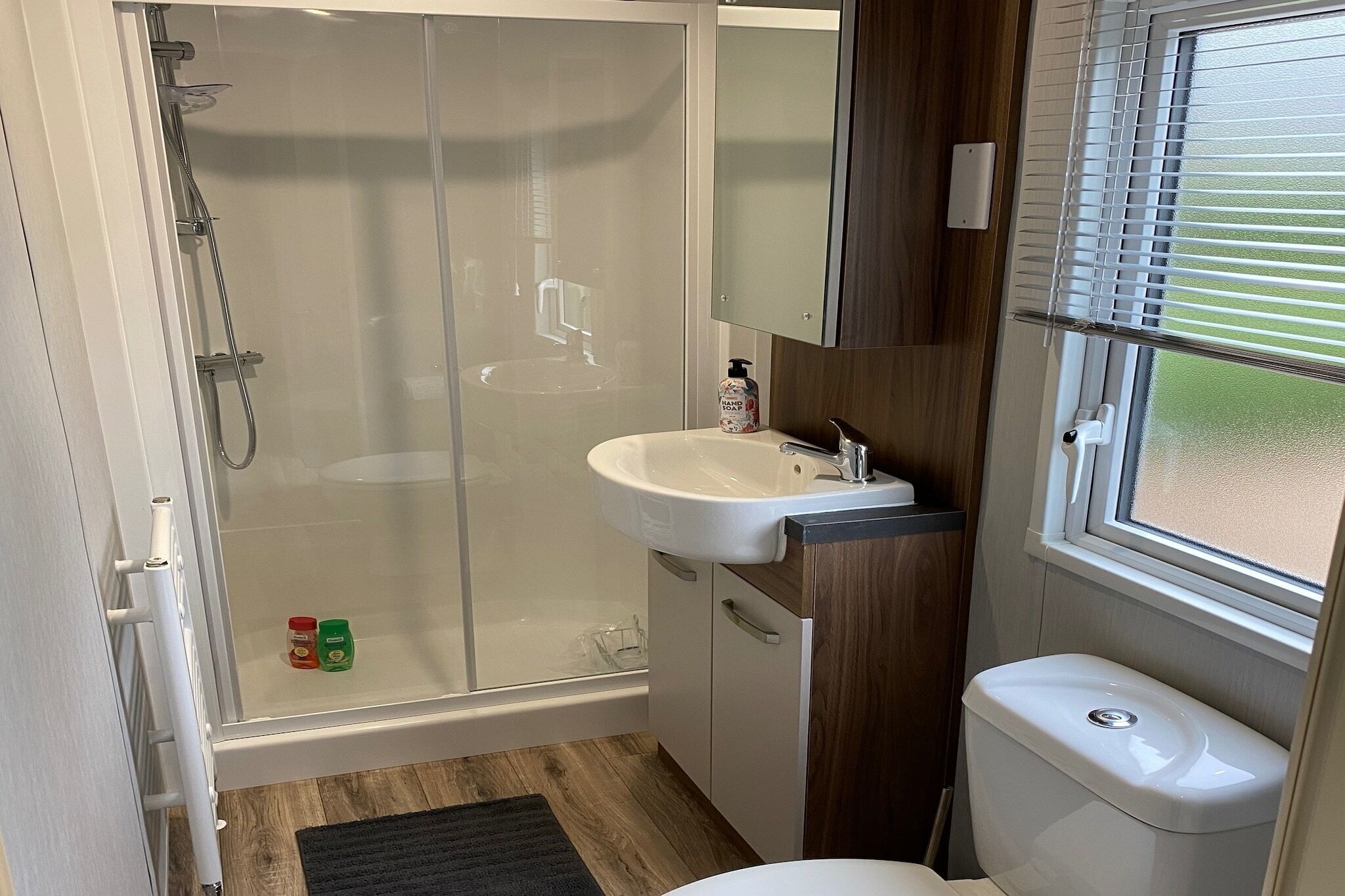 Un baño pequeño con cabina de ducha de vidrio, lavamanos blanco y retrete.