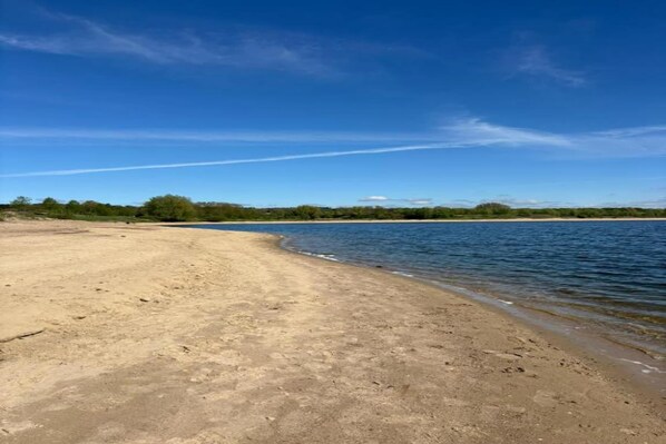 Une plage de sable fin, avec une étendue d’eau calme et un ciel bleu clair.