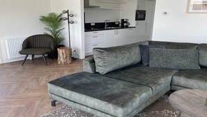 Uma sala de estar moderna com um sofá modular cinza, uma pequena mesa lateral de madeira, uma poltrona verde e um vaso com planta.