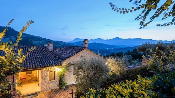 A stone house with a tiled roof, a small patio with outdoor furniture, and a view of distant mountains. - Relaxing Retreat in Le Marche (Monte San Martino)