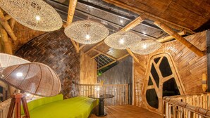 A circular room with a green sofa, a round table, and woven ceiling lamps. - Dreamy Cliffside Bamboo Villa with Pool and View (Klungkung)
