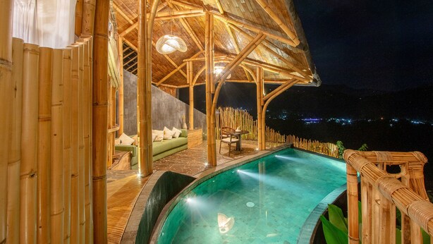 A bamboo-themed pool area with a covered seating area and a view of the night sky. - Dreamy Cliffside Bamboo Villa with Pool and View (Klungkung)