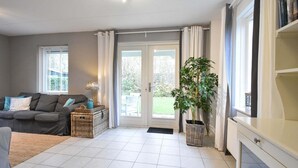 Un salon avec un canapé gris, une petite table avec une lampe, une grande plante en pot et une bibliothèque.