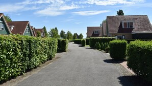 Une rue résidentielle bordée de maisons, un ciel dégagé et des haies bien entretenues.
