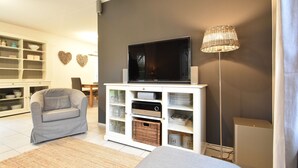 Un salon avec un téléviseur à écran plat posé sur un meuble blanc, un canapé gris, une lampe en osier et un buffet blanc aux portes en verre.