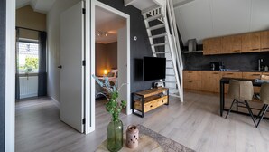 Een moderne keuken met houten kasten, een zwart aanrecht en een televisie. Er is een trap die naar een hoger niveau leidt.