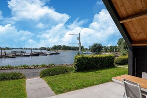A lakeside view with boats docked, a wooden deck, and a pathway leading to a table and chairs. - Beautiful house in Kerkdriel on the waterfront (Kerkdriel)