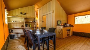 Ein gemütlicher Essbereich aus Holz mit einem Tisch, gedeckt für vier Personen, umgeben von Stühlen. Im Hintergrund ist eine Küchenzeile mit Mikrowelle und Kaffeemaschine zu sehen.