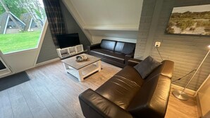 Een moderne woonkamer met een bruine leren bank, een witte salontafel en een tv op een standaard.