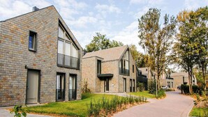 A modern residential building with a brick facade, large windows, and a paved driveway.