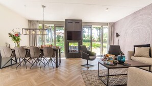A modern living room with a herringbone floor, a fireplace, a dining area with a table and chairs, and a sofa.