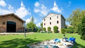 A rustic building with a large garage door, a well-maintained lawn, and various toys scattered on the grass. - Large Group Retreat with Pool (Amandola)