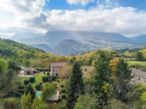 Paisaje rural con una construcción de piedra rodeada de abundante vegetación y una piscina.