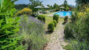 A pool area with a stone pathway, surrounded by lush greenery and flowering plants. - Large Group Retreat with Pool (Amandola)