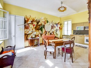 A dining area with a mural, a dining table, chairs, and a kitchen in the background. - Belvilla by OYO Locanda (Portacomaro)