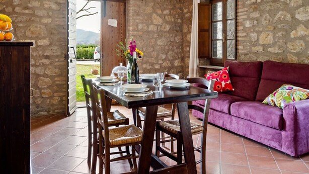 Un comedor con pared de piedra, una mesa de madera dispuesta para dos personas y un sofá morado.