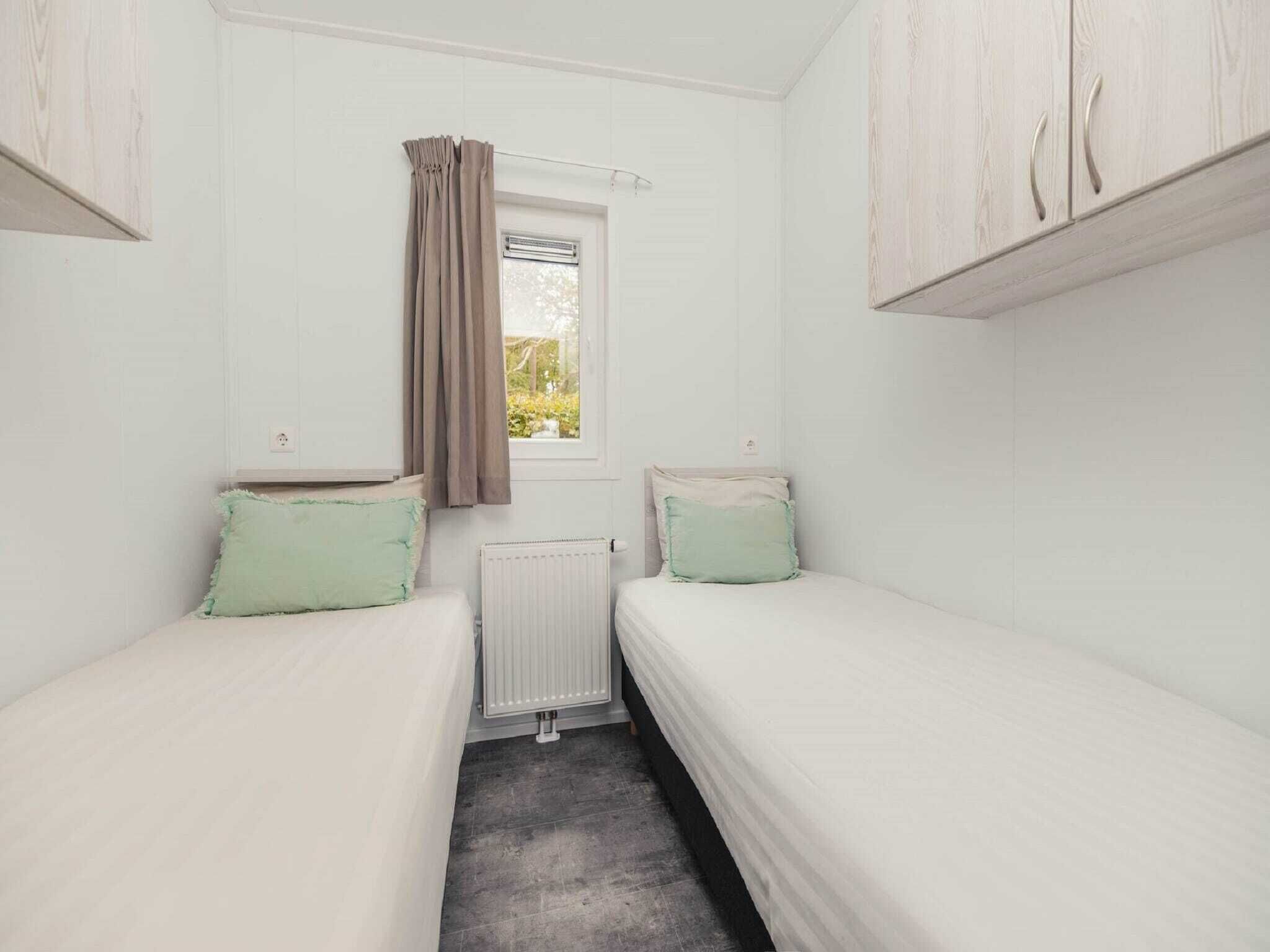 A small, single-room accommodation with two single beds, a window with curtains, and a radiator.