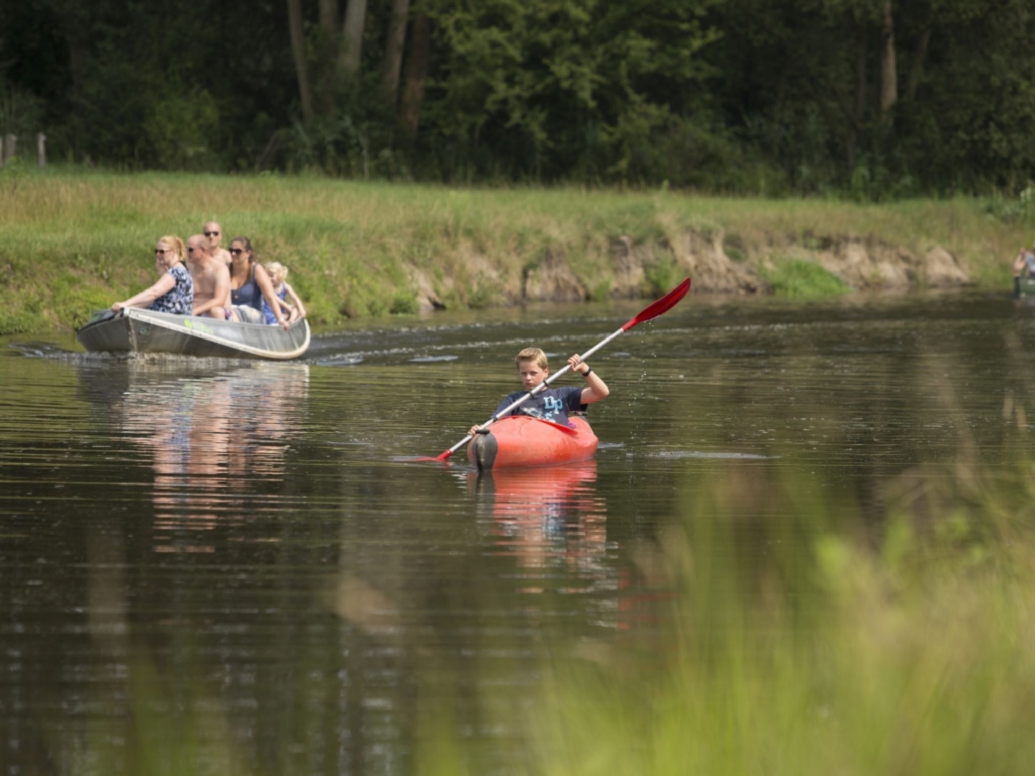 Iemand kajakt op een rivier, met een groep in een boot op de achtergrond.