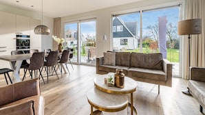 En moderne stue med sofa, spisebord med stole, et køkken og store skydedøre til en have.