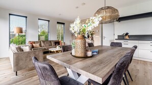 En moderne stue med et træspisebord, mørke læderstole, en sofa og en stor vase med blomster.
