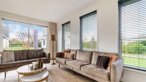 En moderne stue med to sofaer, et sofabord og store vinduer med skodder.